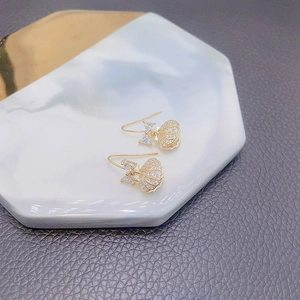 Detailed view of golden shell bow earrings with cubic zirconia on a marble tray