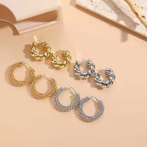 Detailed view of gold and silver twisted hoop earrings with beaded texture on stone board