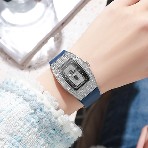 Close-up of diamond-encrusted tonneau watch with blue silicone strap on wrist