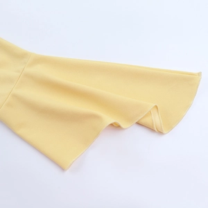 Dettaglio del polsino con volant e taglio a onde sul vestito giallo a maniche lunghe