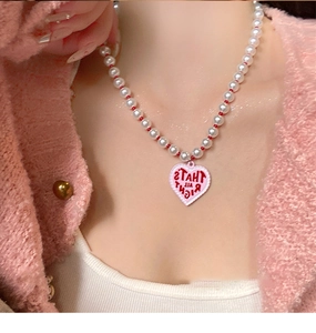 Detail of beaded pearl necklace featuring a pink heart pendant with wave border