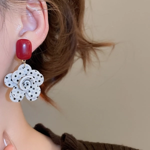Macro detail of burgundy resin earrings with black polka dot flower pendant on model