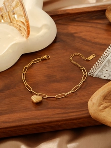Detailed macro of gold paperclip chain bracelet with a textured heart pendant and lobster clasp