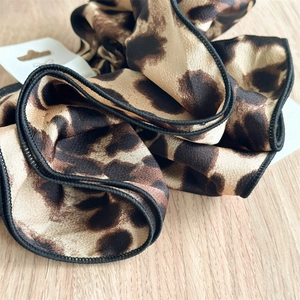 Detailed close-up of leopard print satin scrunchies with elegant black edge piping detail