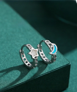 Macro view of asymmetric star and moon hoop earrings with blue and white enamel inlay