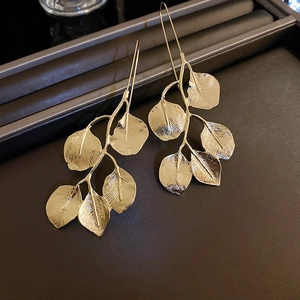 Detail of golden leaf drop earrings with polished metallic finish on dark tray