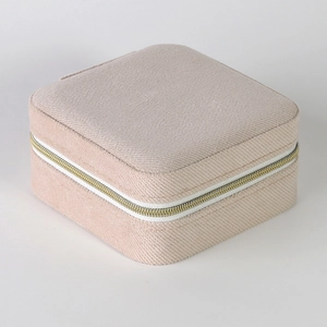 Detailed close-up of a square beige jewelry box featuring a textured fabric and metal zipper