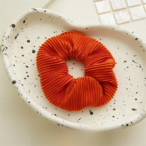 Close-up of orange pleated scrunchie with vertical texture on a ceramic plate