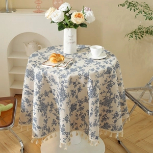 Round beige linen tablecloth with blue floral pattern and tassel edges on breakfast table