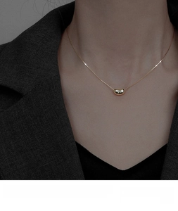 Detailed view of an 18K gold bean pendant necklace on a minimalist link chain