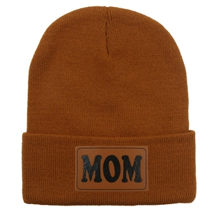 Gros plan du bonnet en tricot caramel montrant l'écusson en cuir MOM et sa texture