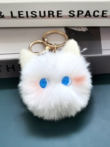 Close-up of white plush cat ball keychain with blue eyes and gold metal clasp