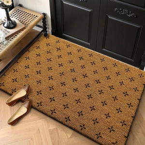 Detailed view of rectangular brown coir doormat with black clover pattern on wood floor