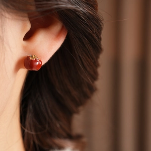 Macro view of model wearing red persimmon earrings with golden leaves and glossy glaze