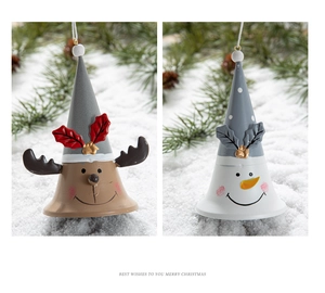 Close-up of reindeer and snowman painted metal bells on snow with festive pine branch background