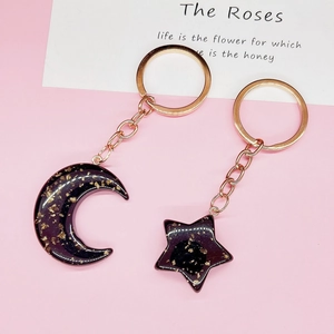 Star and moon acrylic keychains with gold foil glitter on a pink background