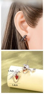 Macro detail of bird stud earrings with red zircon stone and fine chain hanging elements