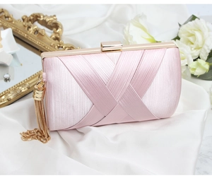 Pink satin evening clutch with elegant gold tassels and metal frame on silk background