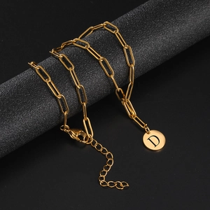 Detail of golden paperclip chain necklace with a round disc pendant featuring letter D