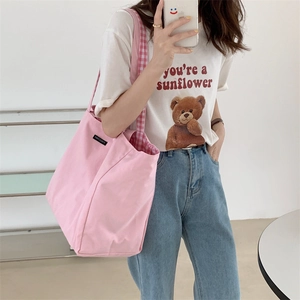 Pink canvas tote bag with plaid lining shown on shoulder for a casual lifestyle look