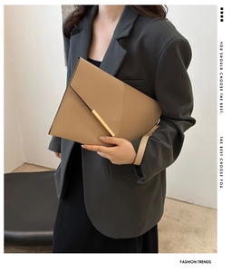 Close-up of a minimalist light brown leather envelope clutch with a gold metal buckle detail