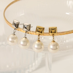 Elegant geometric square gold and silver pearl earrings displayed on glassware