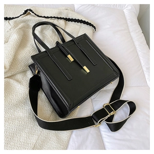 Detail of black structured crossbody bag with wide patterned strap and gold hardware