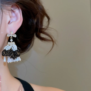 Detailed view of vintage crystal bow and black lace tassel earrings worn by a model