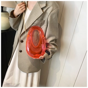 Orange clear acrylic egg-shaped handbag with golden chain strap on a model wearing a suit