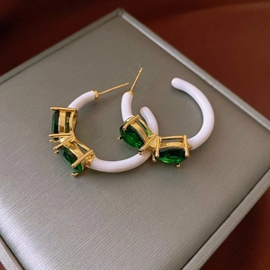Detail of green gemstone and white enamel C-shape floral earrings on jewelry box