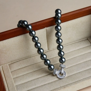 Detailed view of black pearl necklace featuring a round silver rhinestone buckle on a wooden box
