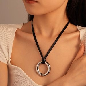Dettaglio del ciondolo a cerchio d'argento minimalista su cordino nero indossato da modella