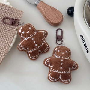 Close-up of cute plush gingerbread man keychains with festive embroidery on a linen mat