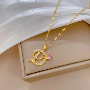 Luxurious gold D-letter pendant necklace with pink gemstone on beige jewelry box