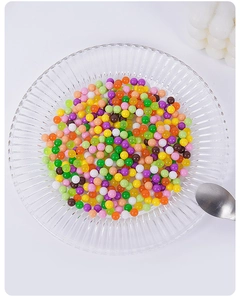 Close-up of colorful mini decorative dessert beads in a clear glass bowl with spoon