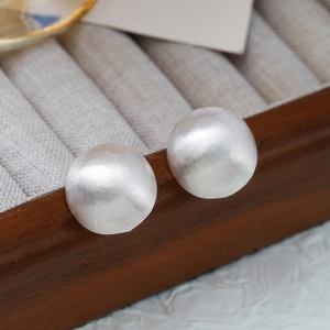 Macro view of matte silver spherical stud earrings with brushed texture on jewelry box