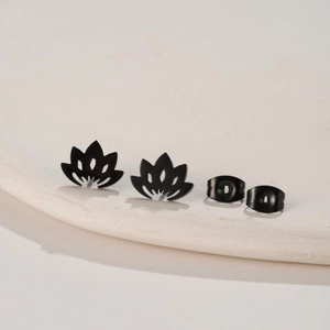 Macro shot of matte black lotus stud earrings with butterfly backings on white plate