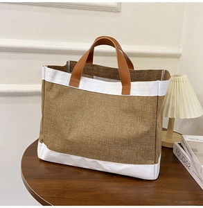 Detail of linen tote bag with brown leather handles and canvas trim on wooden table