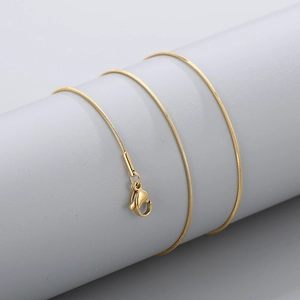 Detail of a gold snake bone chain necklace with a lobster clasp on a grey display stand