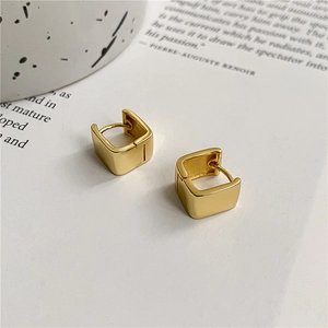 Detail of square gold hoop earrings on a minimalist background with artistic props
