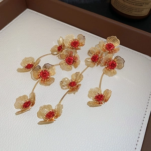 Detailed macro view of golden floral tassel earrings with elegant red center accents