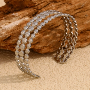 Detailed view of silver triple-row disc bracelet with metallic texture on sand background