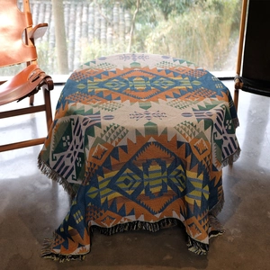 Bohemian geometric knit picnic blanket with tassels displayed on a table in sunlight