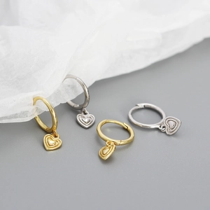 Close-up of gold and silver heart-shaped pendant earrings on light grey background