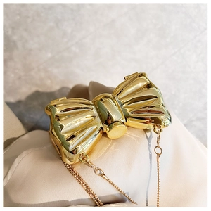 Close-up of a glossy gold bow-shaped hard shell clutch bag with a delicate metal chain