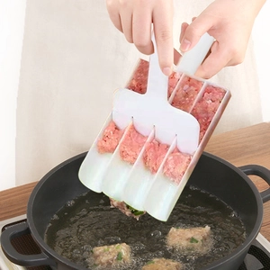 White 4-slot meatball maker tool releasing shrimp balls into a black frying pan