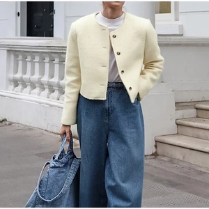 Dettaglio di una giacca di lana bianco crema con jeans a gamba larga in luce naturale