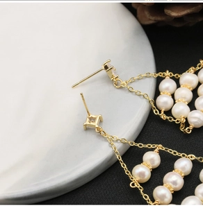 Detailed view of long tassel pearl earrings with gold plating on white marble