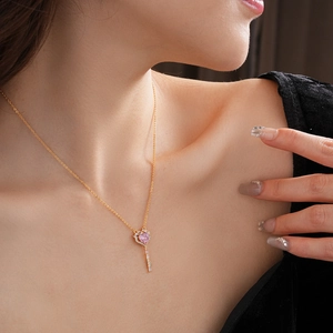 Close-up of gold heart and key pendant necklace with pink zircons on model neck