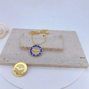 Detail of gold evil eye pendant with blue enamel and textured smiley charm on beige stones